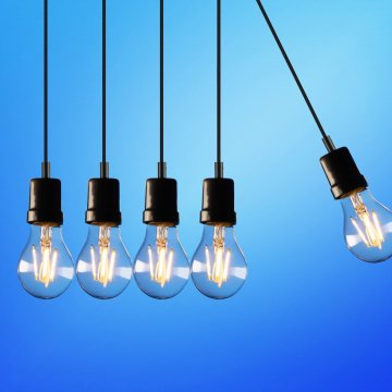 lightbulbs with the power turned on to them hanging down against a blue background